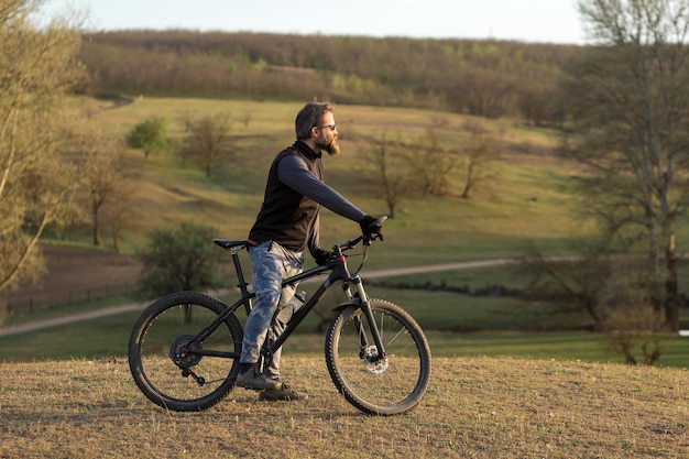 Sport brutale ragazzo barbuto su una moderna mountain bike Ciclista sulle verdi colline in primavera