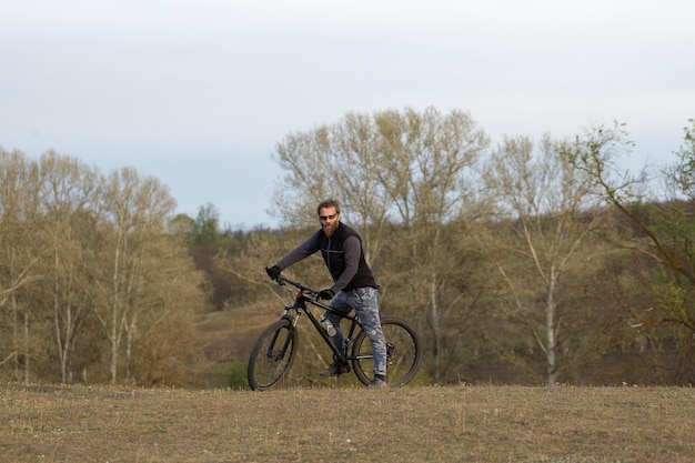 Sport brutale ragazzo barbuto su una moderna mountain bike Ciclista sulle verdi colline in primavera