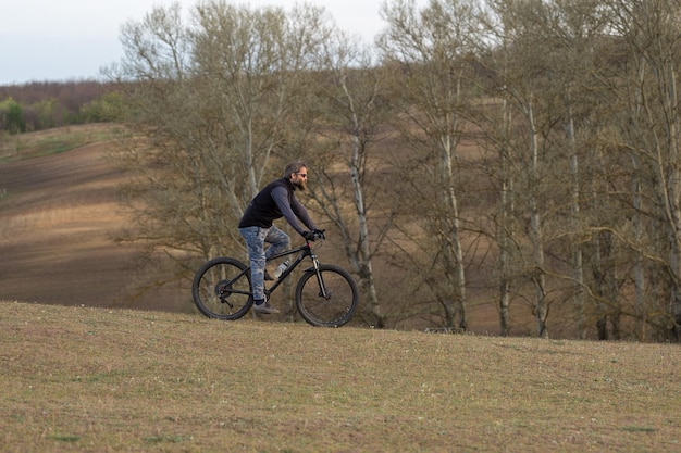 Sport brutale ragazzo barbuto su una moderna mountain bike Ciclista sulle verdi colline in primavera