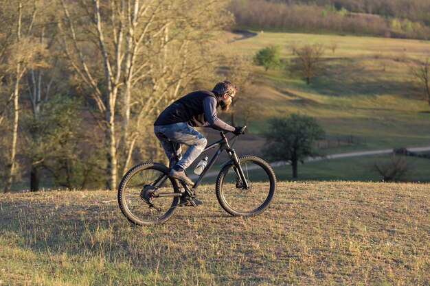 Sport brutale ragazzo barbuto su una moderna mountain bike. Ciclista sulle verdi colline in primavera.