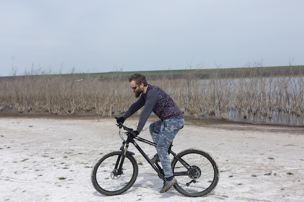 Sport brutale ragazzo barbuto su una moderna mountain bike Un ciclista in un luogo deserto di sale in riva al lago