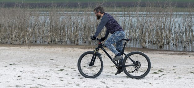 Sport brutale ragazzo barbuto su una moderna mountain bike Un ciclista in un luogo deserto di sale in riva al lago