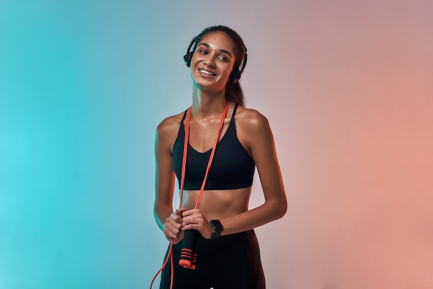 Sport con musica giovane donna sportiva in cuffia che tiene la corda per saltare e guarda la telecamera