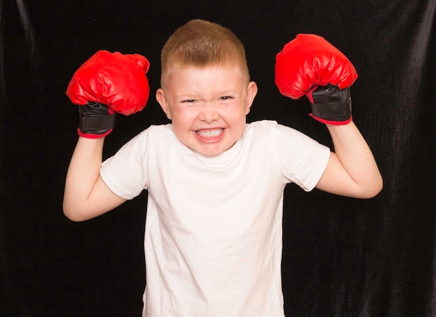 Sport di boxe per bambini un ragazzo con una maglietta bianca e guanti di boxe rossi su uno sfondo nero