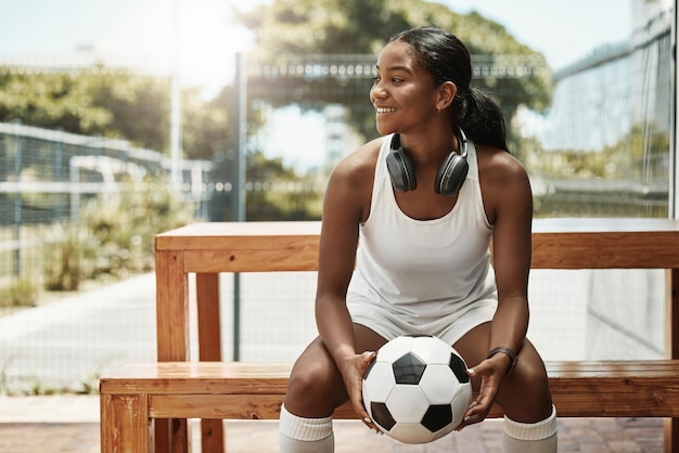 Sport di calcio e una donna in panchina con la palla nel parco cittadino di San Paolo Divertimento fitness e una felice donna di colore in Brasile seduta con in mano un pallone da calcio e guardando una partita sotto il sole estivo con le cuffie