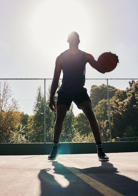 Sport di pallacanestro e uomo in un parco per l'allenamento cardio ed esercizio con una palla durante l'estate Sagoma scura di un atleta professionista con libertà ed energia per uno sport su un campo da basket