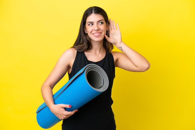 Sport Donna italiana che va a lezioni di yoga isolata su sfondo giallo ascoltando qualcosa mettendo la mano sull'orecchio