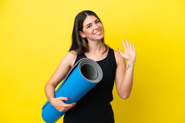 Sport Donna italiana che va a lezioni di yoga isolata su sfondo giallo salutando con la mano con espressione felice