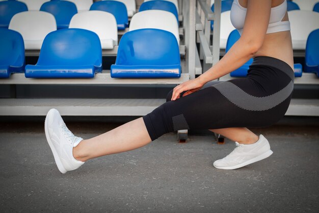 Sport e benessere. Ragazza di forma fisica in scarpe da tennis bianche che fanno allungamento allenamento. Moda donna sportiva con un forte allenamento del corpo muscoloso. Fit femminile che si estende allo stadio all'aperto