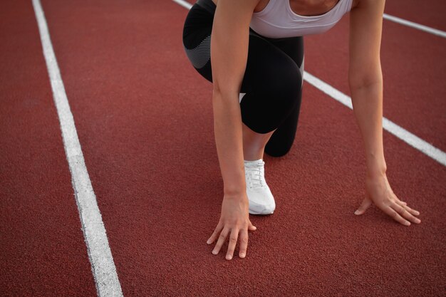 Sport e fitness. Una giovane donna atletica con una maglietta bianca e scarpe da ginnastica bianche si prepara a correre sulla pista dello stadio stadium