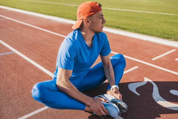 Sport e persone Atleta caucasico che fa esercizi di stretching seduto sulla pista da corsa Runner uomo seduto sulla pista da corsa con i piedi uniti preparandosi per una corsa o rilassarsi dopo l'allenamento