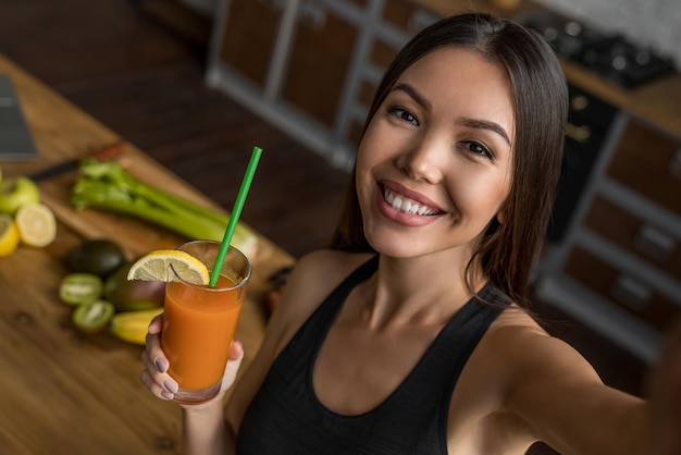 Sport femminile che beve frullato e si fa selfie in cucina