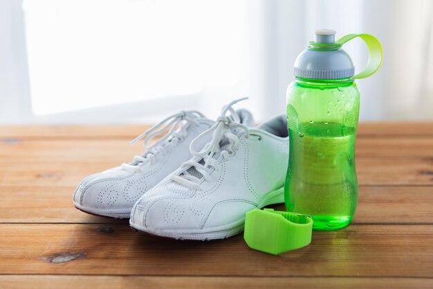 sport, fitness, stile di vita sano e concetto di oggetti - primo piano di scarpe da ginnastica, bracciale e bottiglia d'acqua su pavimento in legno