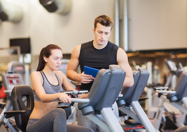 sport, fitness, stile di vita, tecnologia e concetto di persone - donna con trainer che si allena sulla cyclette in palestra