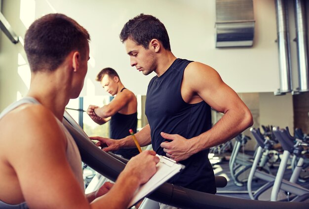 sport, fitness, stile di vita, tecnologia e concetto di persone - uomini con personal trainer che si esercitano sul tapis roulant in palestra