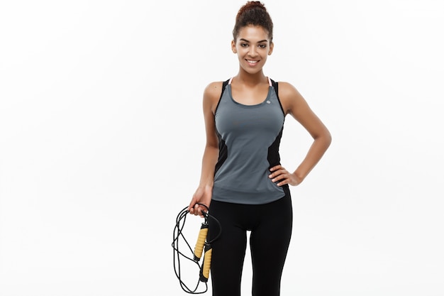 Sport, formazione, stile di vita e fitness concetto - ritratto di bella donna felice African American esercitando con corda di salto.