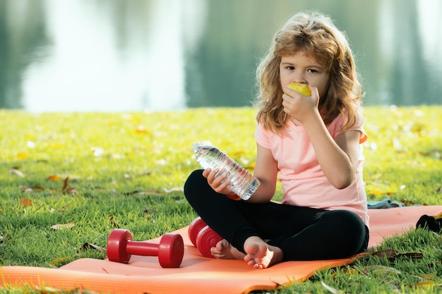 Sport kids boy Il bambino mangia il resto della mela sul tappetino sportivo dopo gli esercizi sportivi all'aperto nel parco