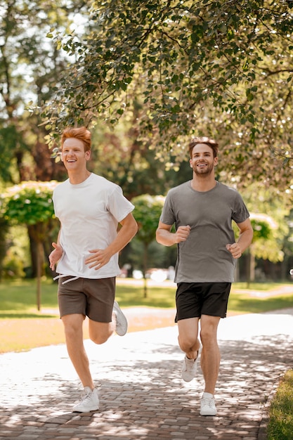 Sport, salute. Due amici sportivi energici sorridenti in maglietta e pantaloncini che corrono nel parco in una mattina di sole estivo