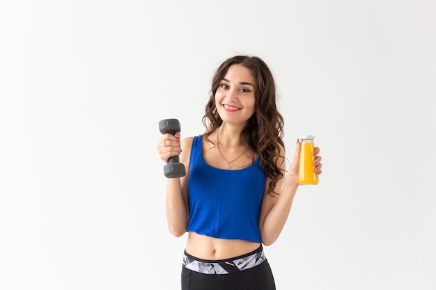 Sport, stile di vita sano, concetto di persone - giovane donna con un manubrio in mano e una bottiglia di succo in un'altra mano.