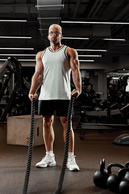 Sport. Uomo forte che si esercita con corde da battaglia in palestra con Atleta che fa allenamento con la corda di battaglia in palestra Sfondo sportivo drammatico.