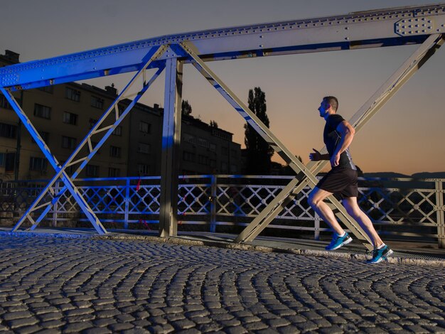 sport urbani, giovane uomo sano che fa jogging attraverso il ponte della città al mattino presto di notte