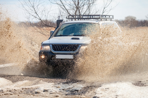 Sport Utility Vehicle su strada sterrata all'inizio della primavera facendo schizzi da una pozzanghera