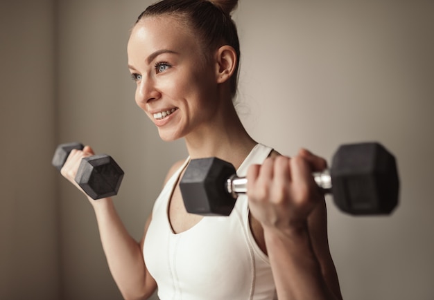 Sportiva allegra che si esercita con i dumbbells a casa