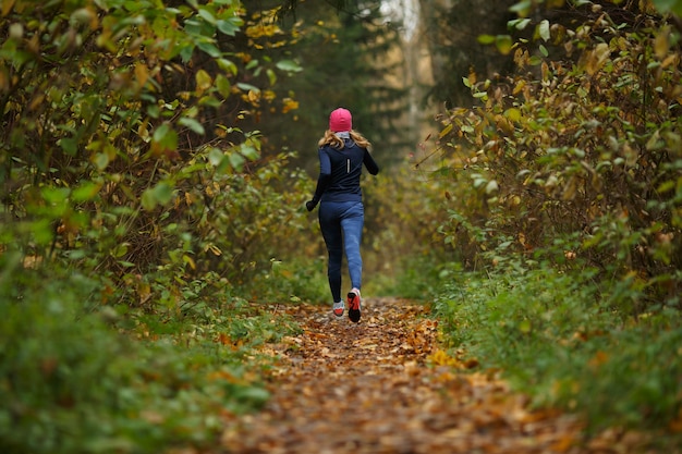 Sportiva bionda corre in pista nel parco autunnale