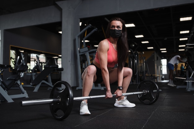 Sportiva che indossa una maschera medica che fa squat di sumo con bilanciere