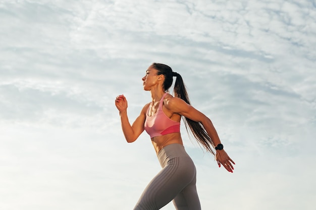 Sportiva con capelli lunghi che corrono all'aperto contro i cieli Jogger femminile sottile che corre sul tetto