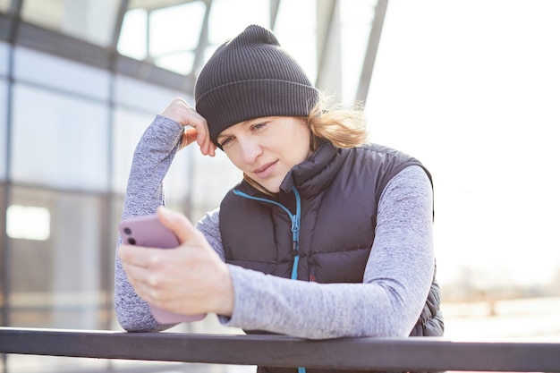 Sportiva di mezza età sorridente felice utilizzando lo smartphone in città