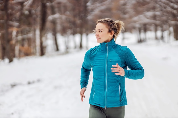 Sportiva in forma che fa jogging nella natura su un tempo nevoso. Freddo, neve, vita sana, fitness