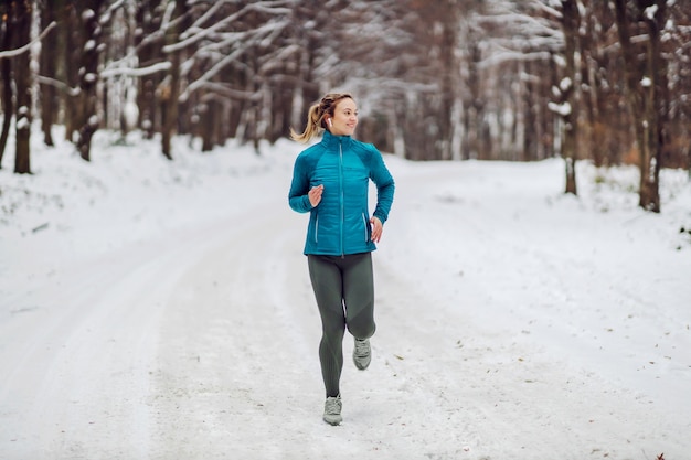 Sportiva jogging nei boschi in una fredda giornata invernale nevosa. Freddo, neve, vita sana, fitness, foresta