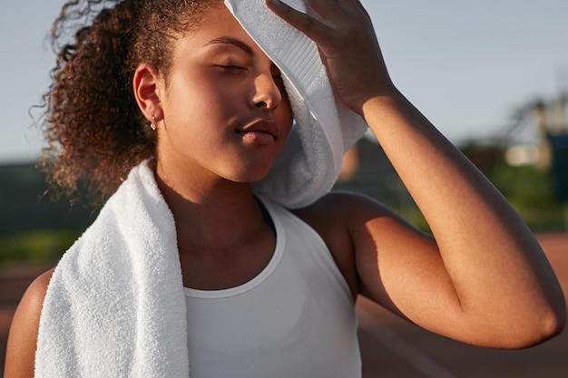 Sportiva nera stanca che pulisce il viso con un asciugamano