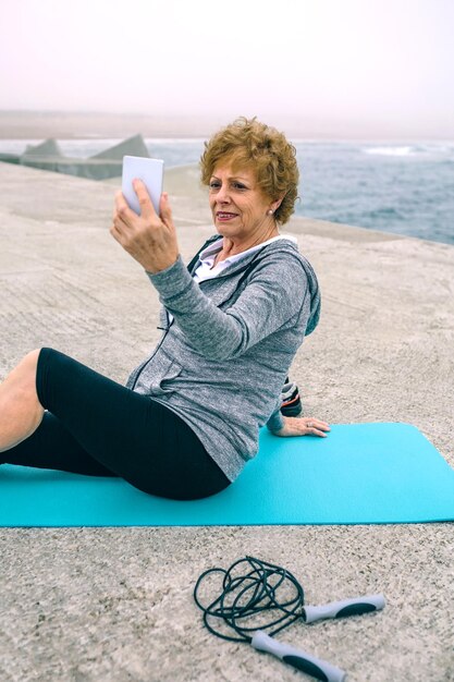 Sportiva senior che prende selfie dal molo del mare