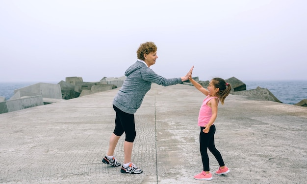 Sportiva senior e bambina danno il cinque al molo del mare