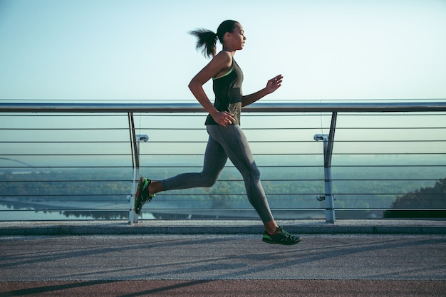 Sportiva seria che corre sul ponte in abiti sportivi