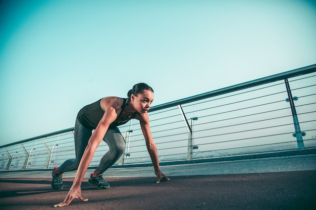 Sportiva sicura che mette mani e piedi a terra e sembra pronta per correre