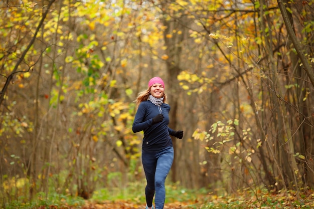 Sportiva snella che corre al parco in autunno