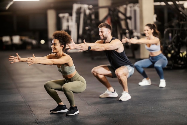 Sportivi muscolosi che fanno squat di resistenza in una palestra insieme