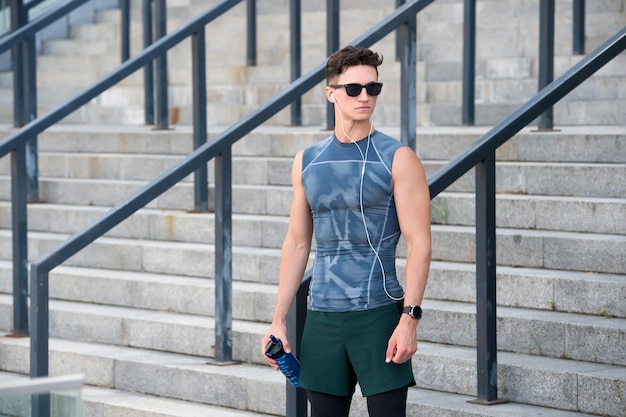Sportivo che indossa occhiali da sole e tecnologia del dispositivo indossabile guarda durante l'allenamento. Atleta muscolare che si esercita all'esterno. Uno stile di vita sano. in attesa di istruttore di fitness.