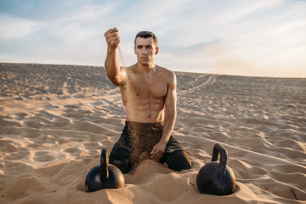 Sportivo che si siede sulla sabbia dopo l'allenamento nel deserto al giorno pieno di sole. Forte motivazione nello sport, allenamento di forza all'aperto