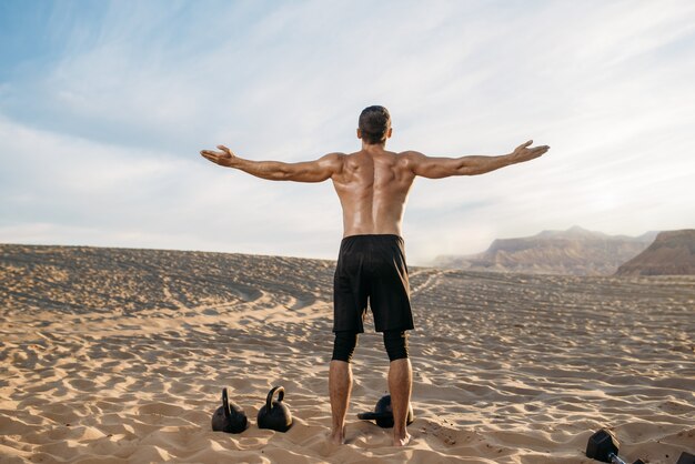 Sportivo facendo esercizi con i pesi nel deserto al giorno pieno di sole, vista posteriore. Forte motivazione nello sport, allenamento di forza all'aperto