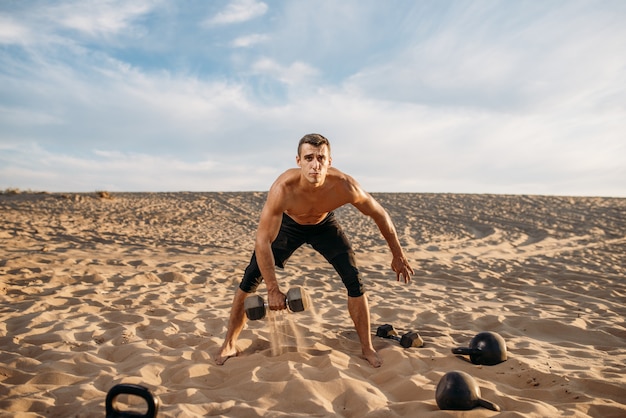 Sportivo facendo esercizi con manubri nel deserto al giorno pieno di sole. Forte motivazione nello sport, allenamento di forza all'aperto