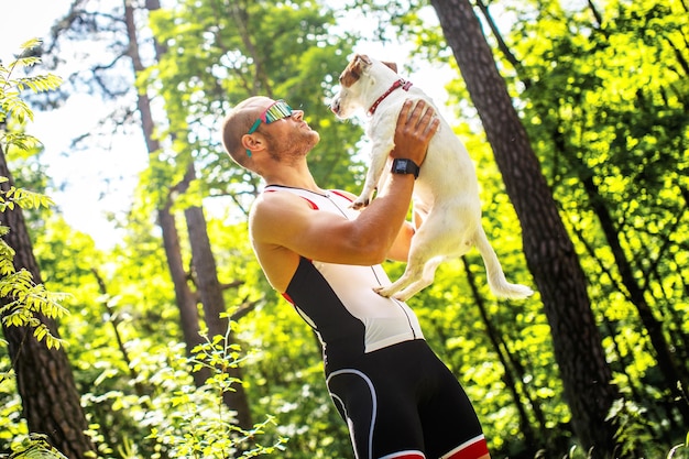 Sportivo in abiti sportivi e occhiali da sole con il suo cagnolino nella foresta verde.