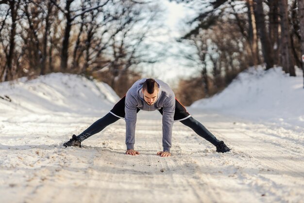 Sportivo in forma in piedi sul sentiero innevato in natura e facendo esercizi di riscaldamento e stretching. Fitness invernale, flessibilità, vita sana