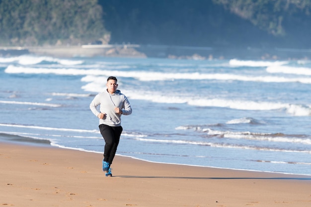 Sportivo latino che corre sulla sabbia in riva al mare