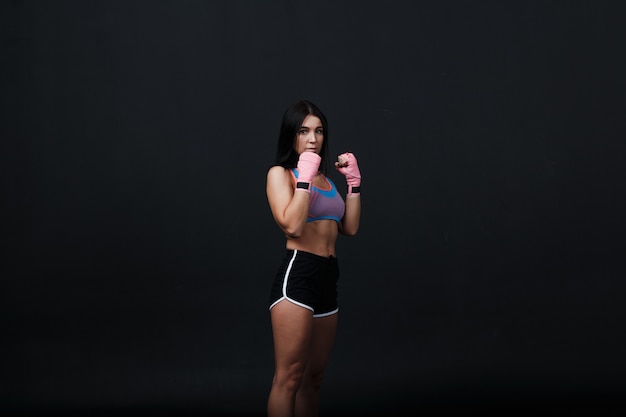 Sportivo muay thai boxer donna in posa in studio di formazione a sfondo nero.