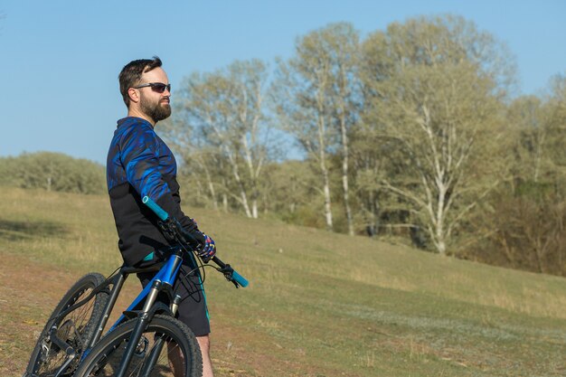 Sportivo ragazzo barbuto brutale su una moderna mountain bike Bella vista dalla montagna