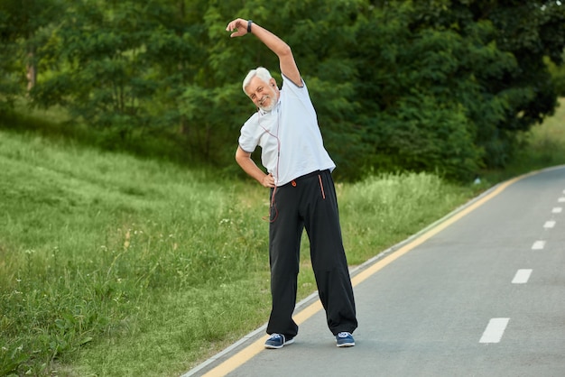 Sportivo senior sorridente positivo che fa allungamento di mattina.